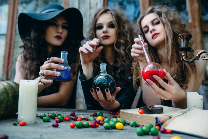 Three witches are sitting at the table and prepared the potion on the eve of Halloween, stock photo