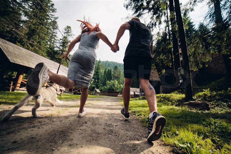 Couple runs on road in the nature with dog to a house, stock photo