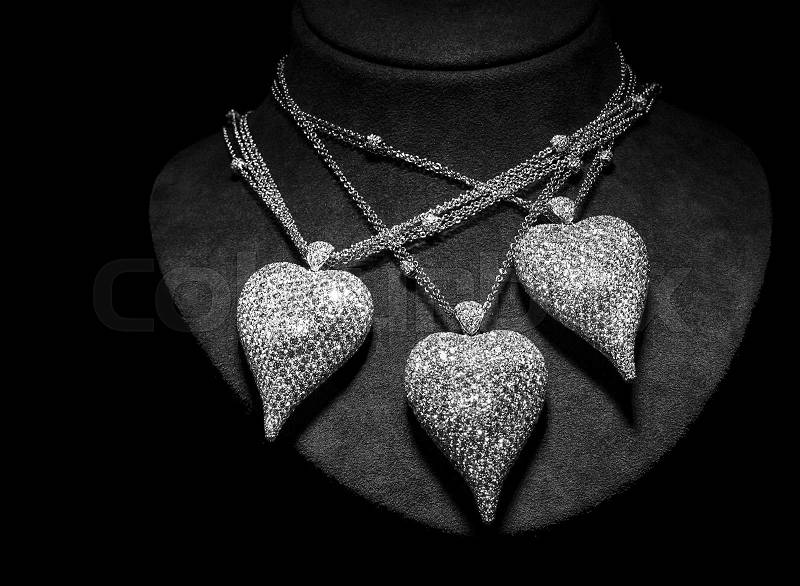 Three necklaces made of white gold or silver on a stand. Heart-shaped pendants with diamonds. Luxury women accessories, stock photo