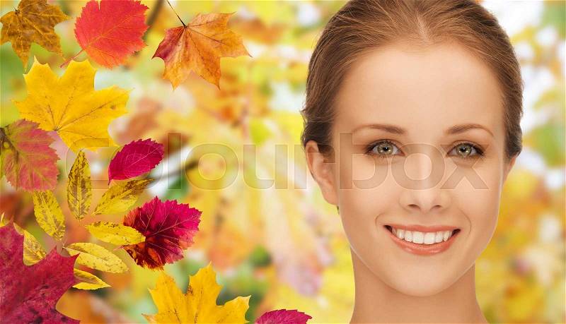 Beauty, people and season concept - beautiful young woman face over autumn leaves background, stock photo