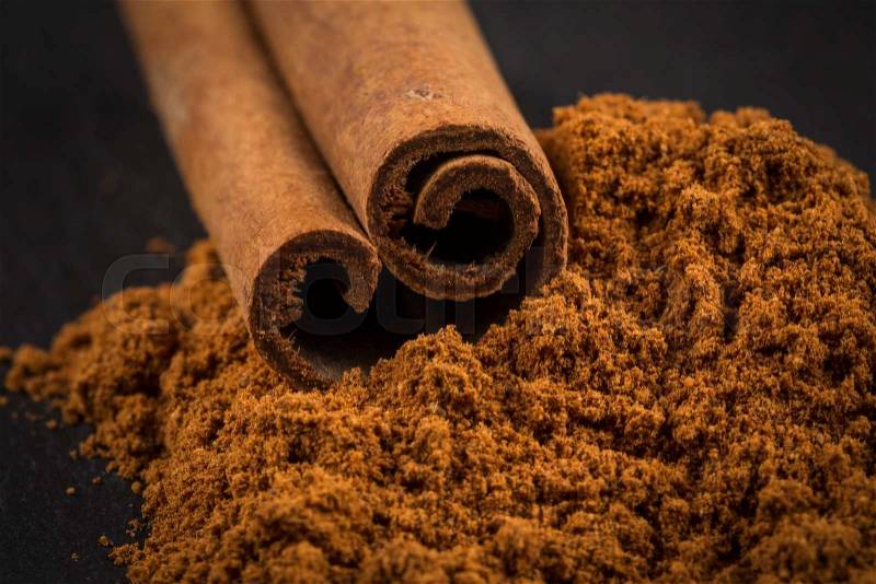 Cinnamon sticks with cinnamon powder on stone plate background, stock photo