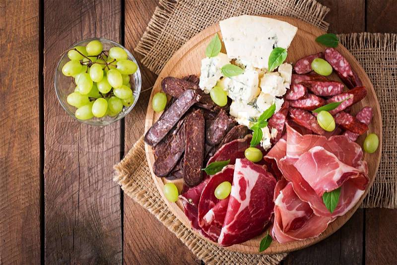 Antipasto catering platter with bacon, jerky, sausage, blue cheese and grapes on a wooden background, stock photo