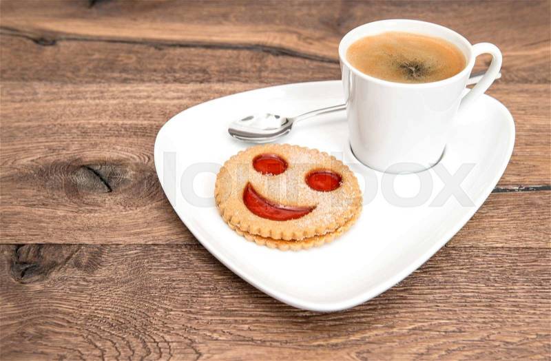 Cup of black coffee with smiled cookie on wooden background. Funny breakfast, stock photo