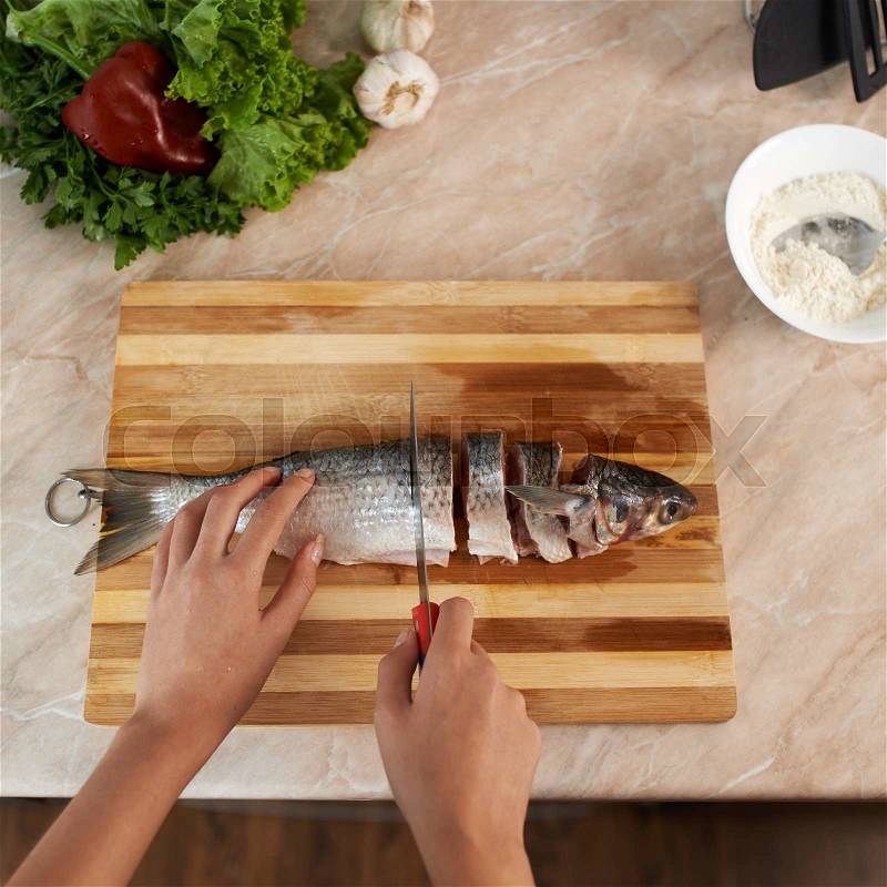Girl cut slice of fish to cook dinner, stock photo