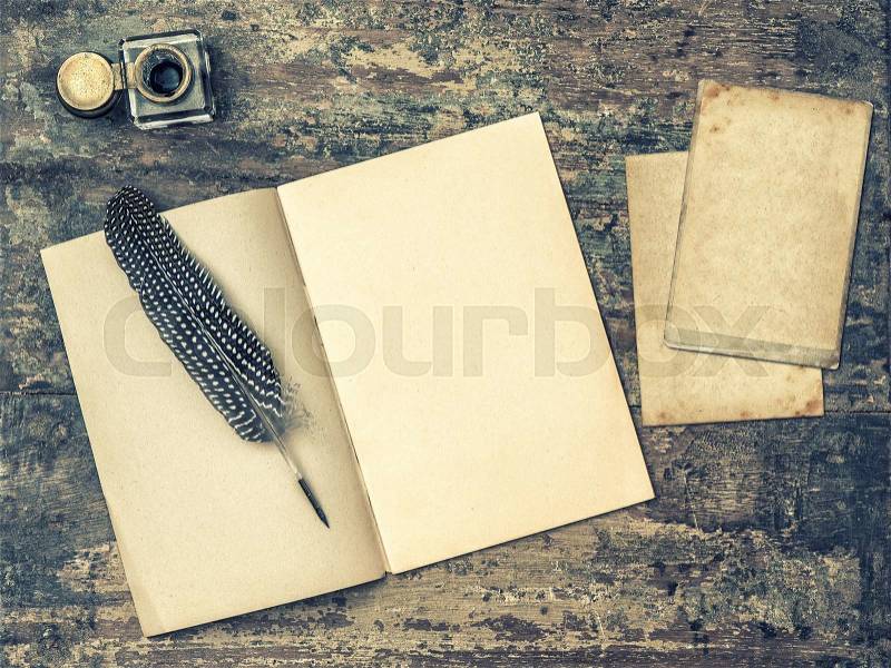 Open book, antique writing tools feather pen and inkwell on textured wooden background. Vintage style toned picture, stock photo