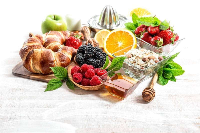 Breakfast table setting with croissants, muesli, fresh berries, fruits orange, apple, milk. Healthy nutrition, stock photo