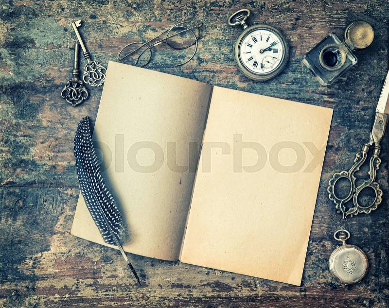 Open book and vintage writing on wooden table. Feather pen, inkwell, keys on textured background. Retro style toned picture with vignette, stock photo