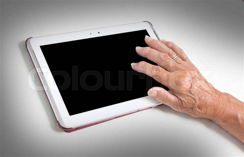 Hand of senior lady relaxing and reading the screen of her tablet, black screen visible, stock photo