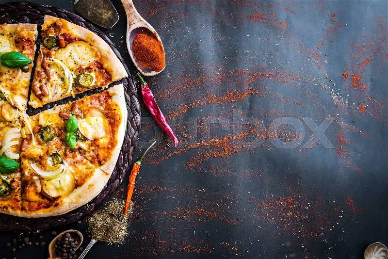 Tasty pizza on a black background with spices and herbs, stock photo