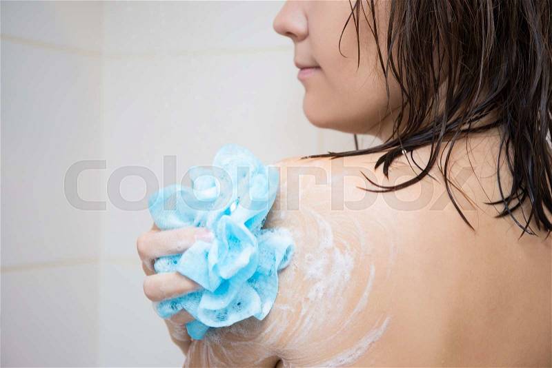 Hygiene concept - young woman washing her shoulder with sponge in shower, stock photo