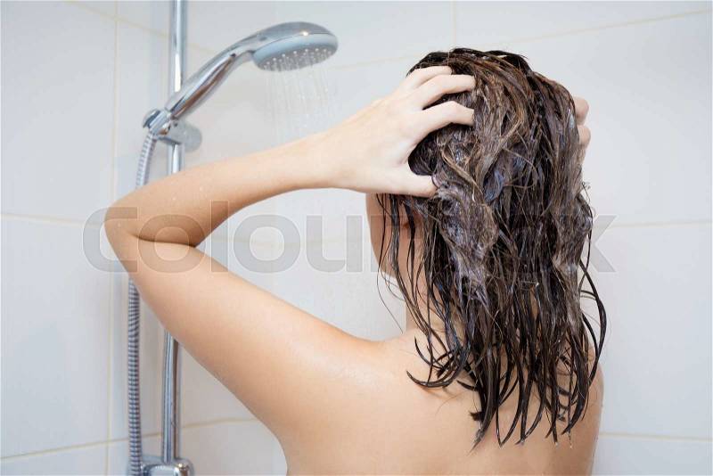 Body care concept - back view of young woman washing her hair with shampoo in shower, stock photo