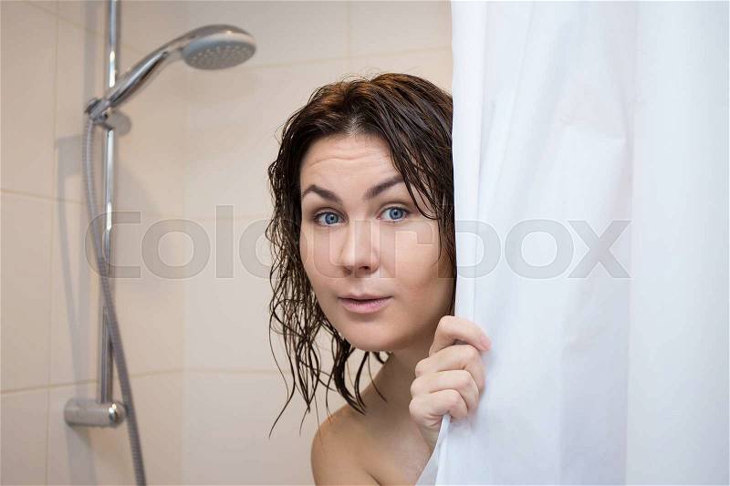 Cute scared young woman hiding behind shower curtain, stock photo