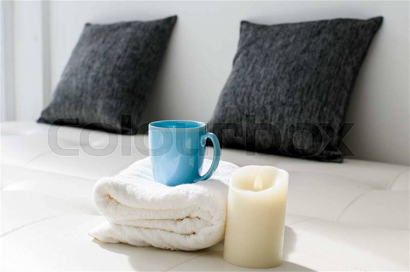 Cozy look, candle and coffee mug on white towel in living room, stock photo