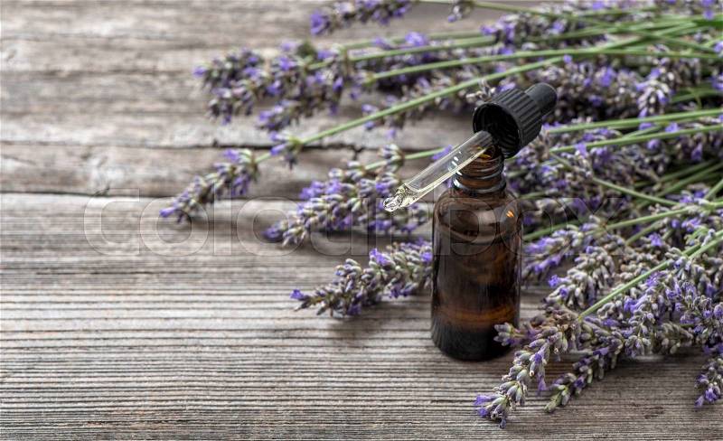Herbal oil and lavender flowers bouquet on wooden background. Alternative home medicine, stock photo