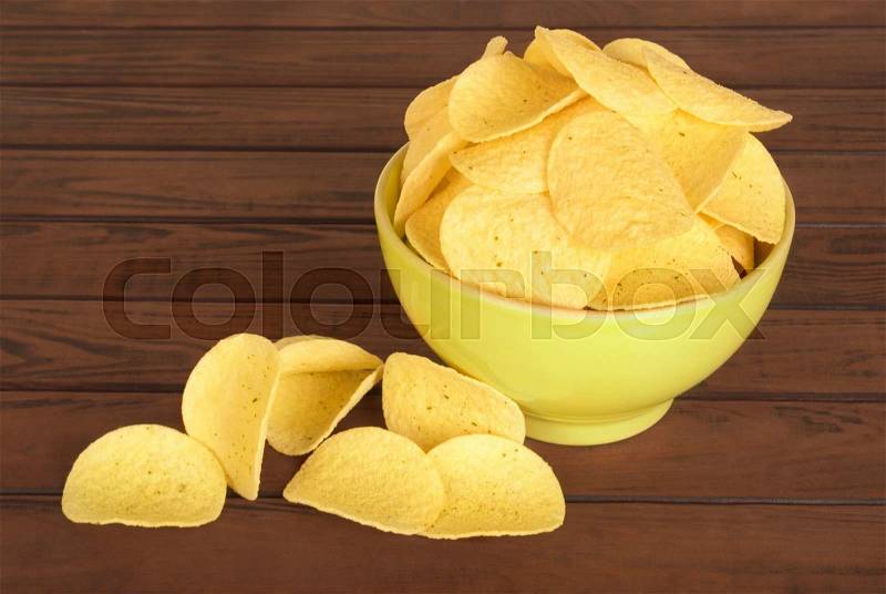 Tasty potato chips in green bowl on wooden table, stock photo
