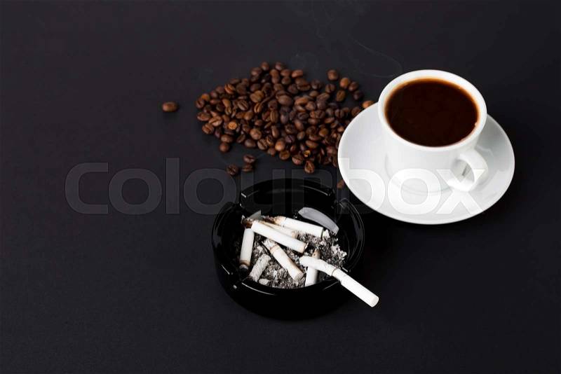 White cup of coffee with ashtray and coffee beans on the black background, stock photo