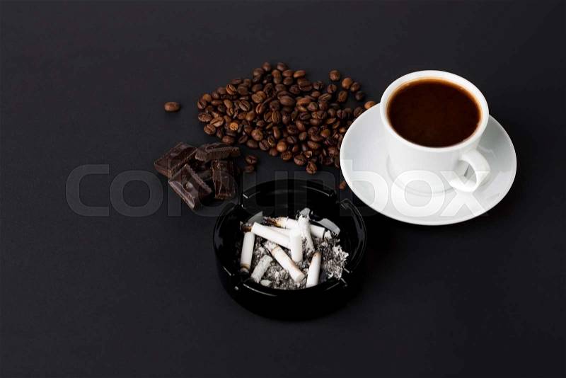 White cup of coffee with ashtray and coffee beans with chocolate on the black background, stock photo