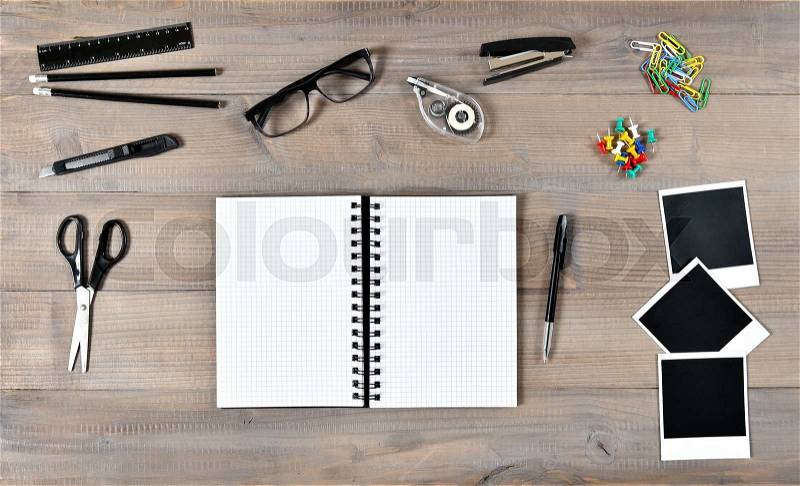 Office and school supplies over wooden desk background. Open book, polaroid photo frames and writing tools, stock photo