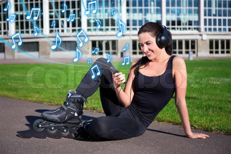 Pretty woman in roller skates sitting and listening music in summer park, stock photo