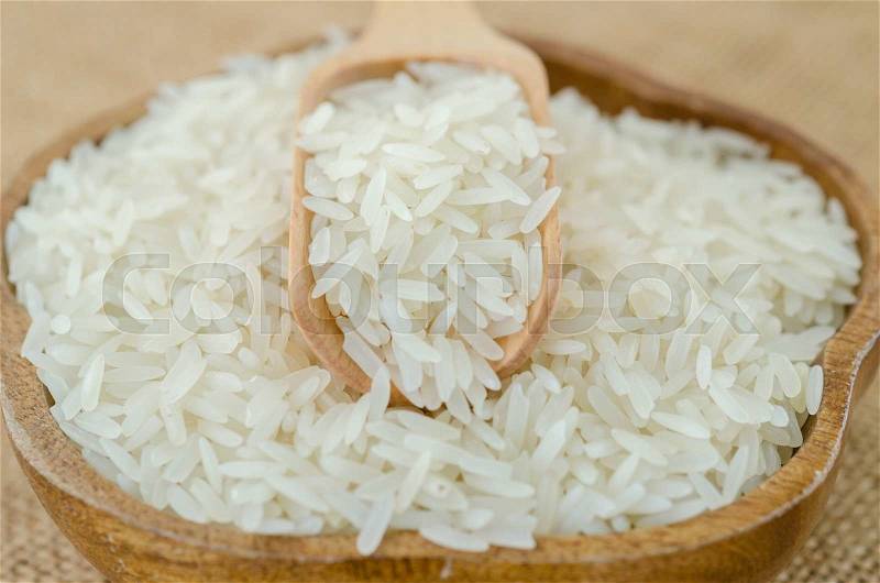 Raw rice and wooden spoon in wooden bowl on sack background, stock photo
