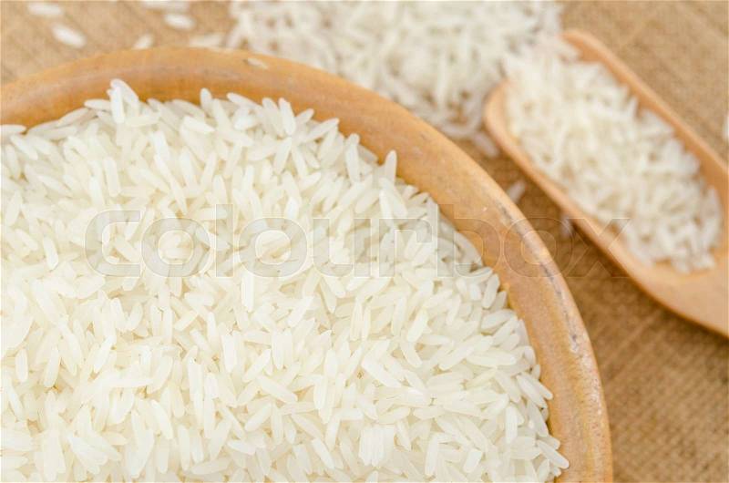 Raw white rice in wooden bowl on sack background, stock photo
