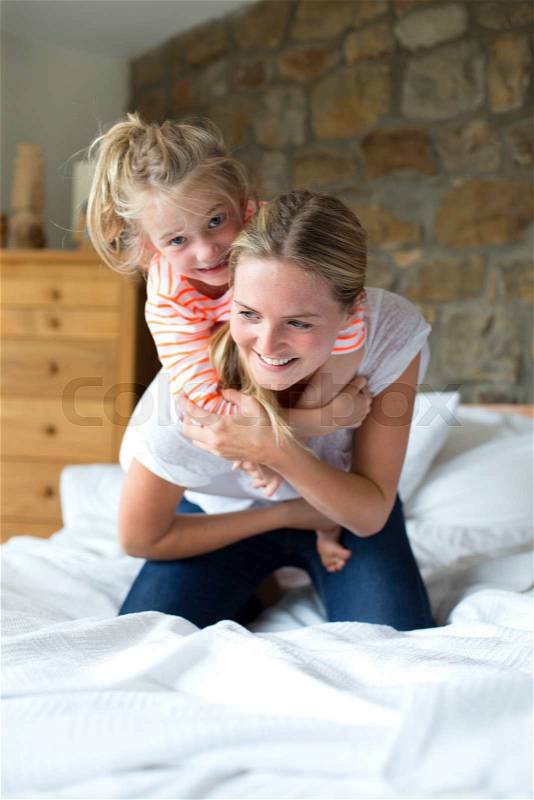 Mother and daughter playing on a bed at home, stock photo