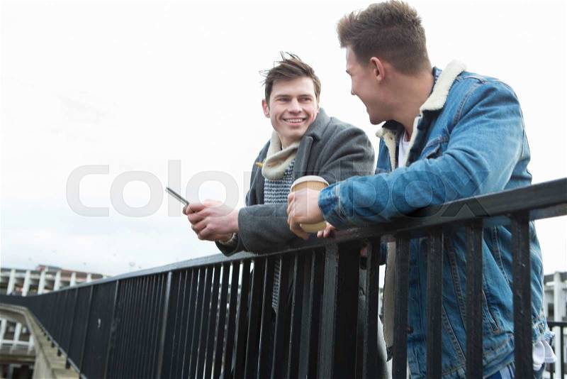 Two young men talking in the city. One is holding a smartphone, the other is holding a disposable coffee cup, stock photo