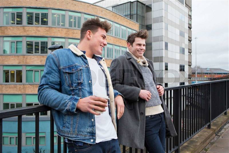 Two young men talking in the city. One is holding a disposable coffee cup, stock photo
