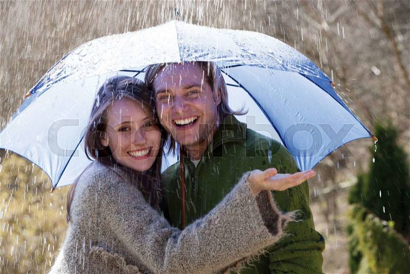 Young couple enjoying the rain under an umbrella , stock photo