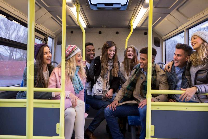 Group of young adults sitting together at the back of the bus. They are laughing and talking, stock photo