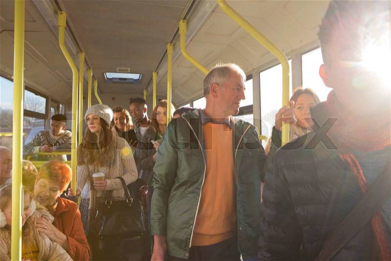 Different people can be seen travelling on the bus. Some are talking to other people, others are using technology or looking out the window. , stock photo
