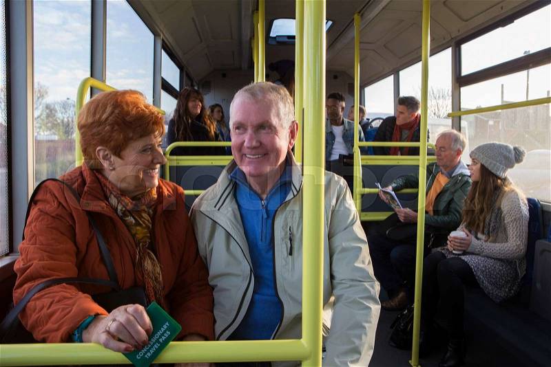 Senior couple travelling on the bus. There are other people sat on the bus who are in the background. , stock photo