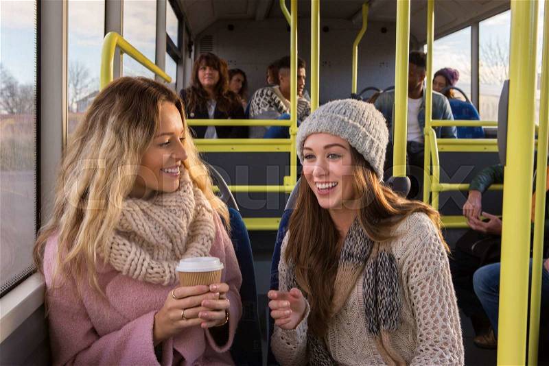 Two women talking as they travel on a bus together, stock photo