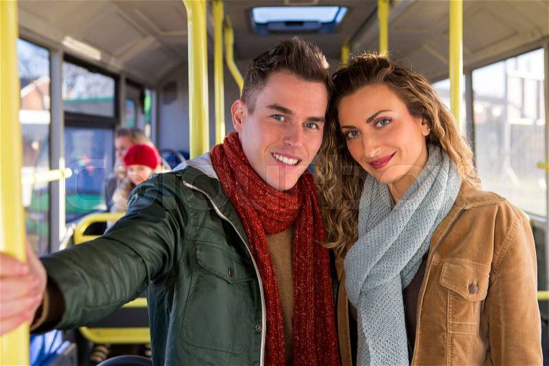 Young couple posing on a bus for the camera. They are standing up and there are people sitting on the bus in the background, stock photo