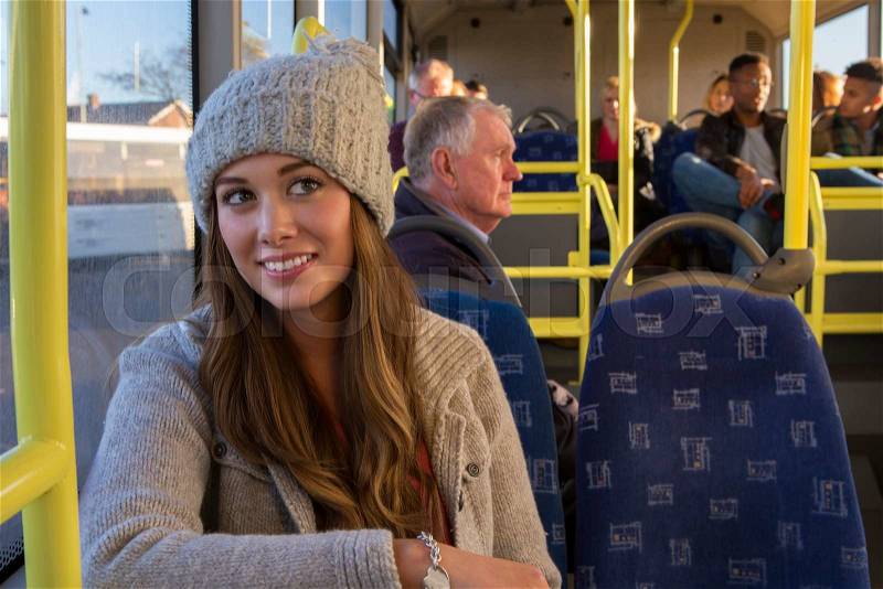Young woman sitting on the bus. She is leaning against the window and smiling to the side, stock photo