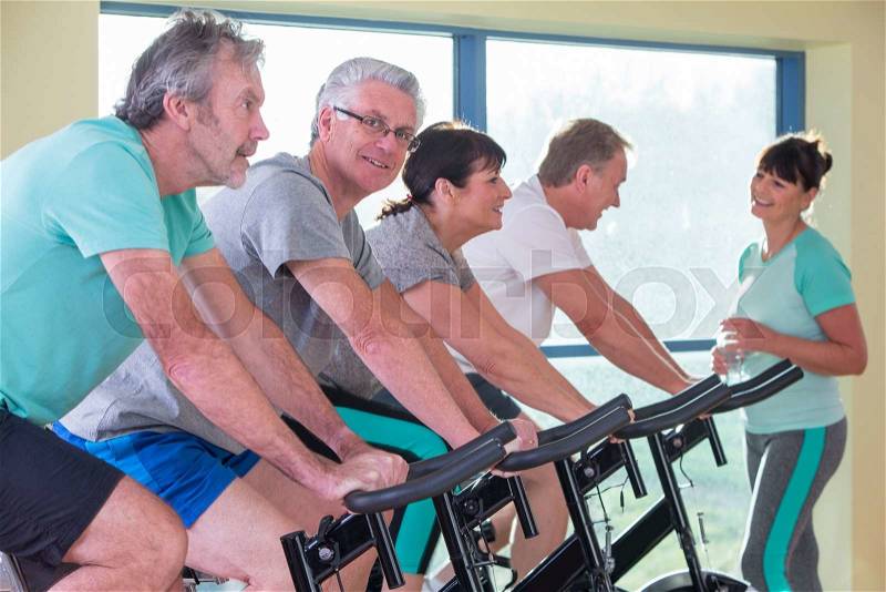 A group of seniors using the spinning bikes at the gym, stock photo