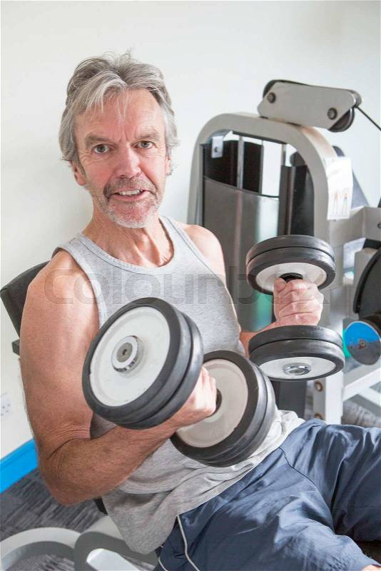 Senior man posing with weights at the gym, stock photo