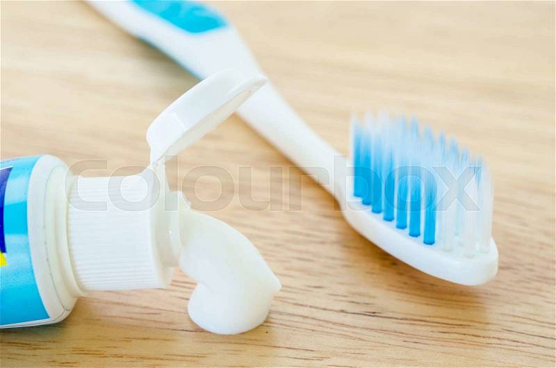 White toothpaste spill out a tube of toothpaste and toothbrush on wooden background, stock photo