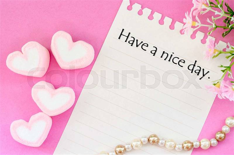 Have a nice day written with sweet heart shape of pink marshmallows with flower on pink background, stock photo