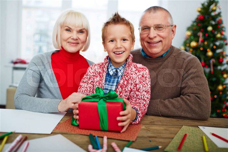 Happy boy with gift-box looking at camera with his grandparents near by, stock photo