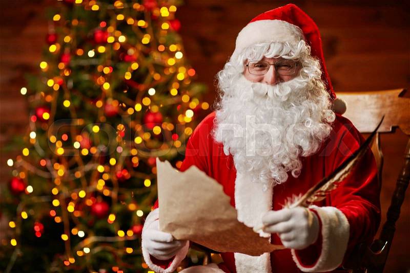Senior man in costume of Santa Claus writing Christmas letter, stock photo