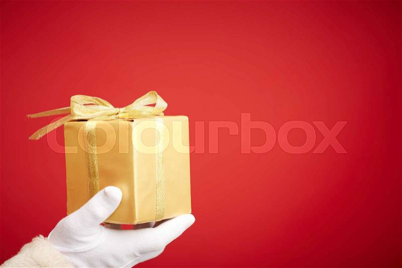 Gloved Santa hand holding giftbox wrapped into golden paper, stock photo