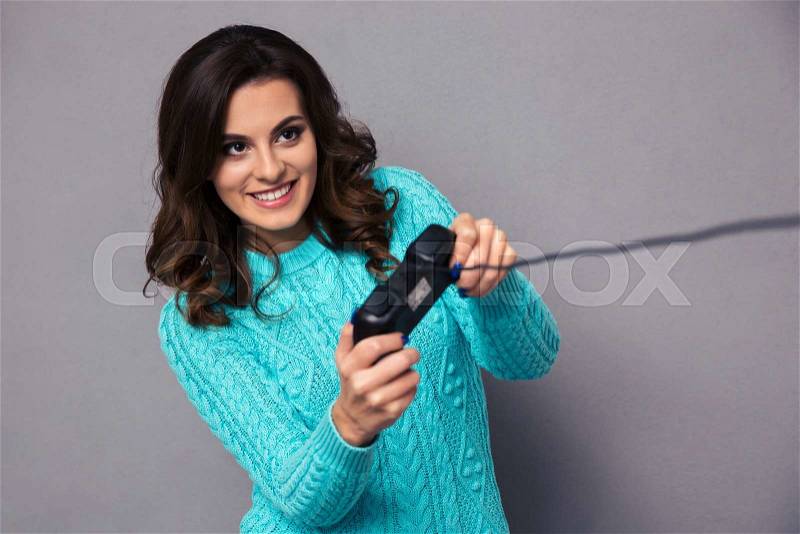 Portrait of a happy woman gaming with joystick over gray background, stock photo