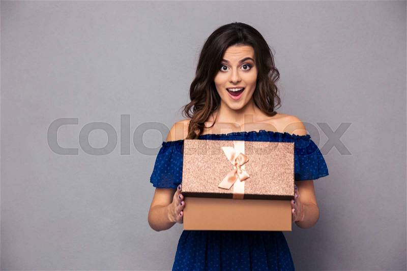 Portrait of a happy woman opening gift box and looking at camera over gray background, stock photo