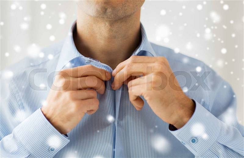 People, business, fashion and clothing concept - close up of man dressing up and fastening buttons on shirt at home over snow effect, stock photo