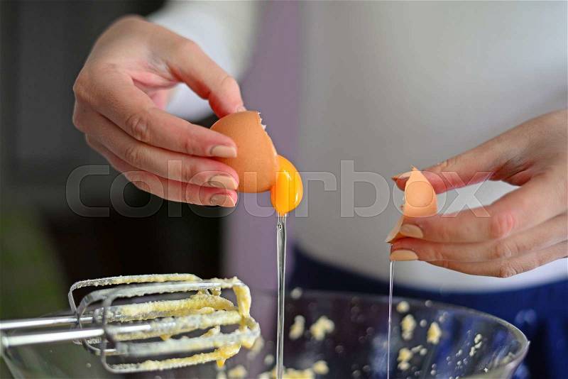 Closeup of a pair of hands cracking an egg into a glass bowl, stock photo