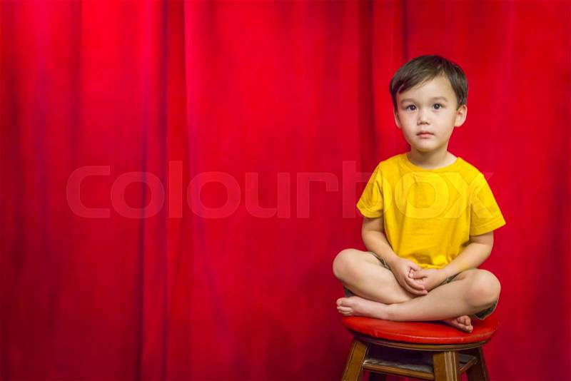Handsome Mixed Race Boy Sitting on Stool in Front of Red Curtain, stock photo