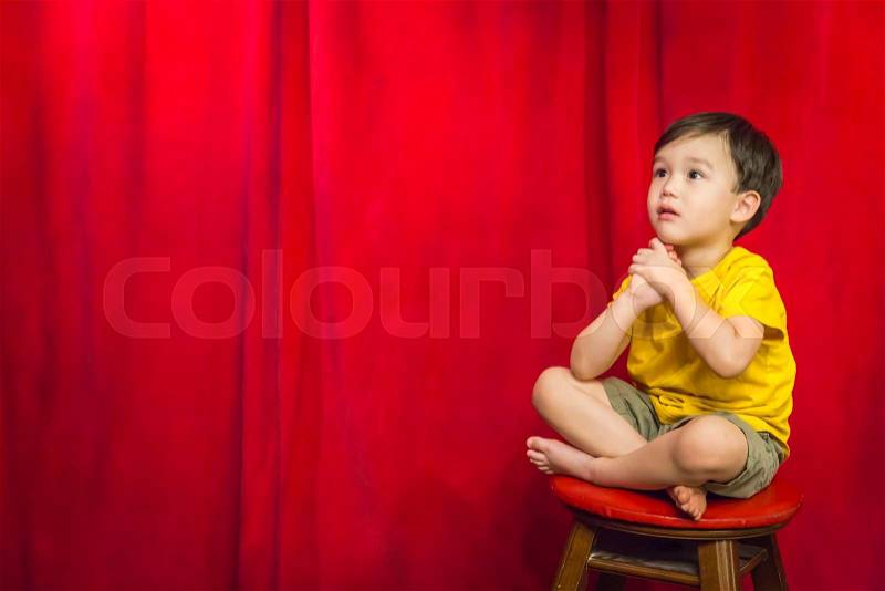 Handsome Mixed Race Boy Sitting on Stool in Front of Red Curtain, stock photo