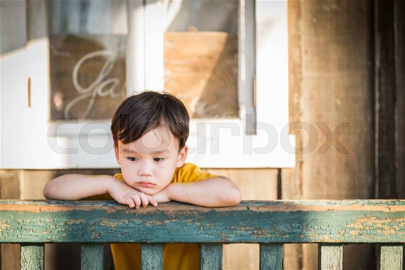 Melancholy Mixed Race Boy Leaning on Porch Railing, stock photo