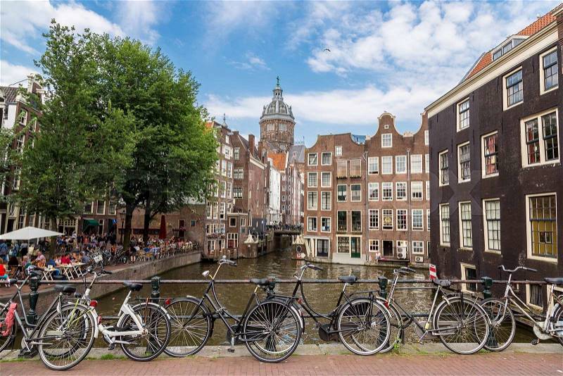 Bicycles on a bridge over the canals of Amsterdam, Netherlands in a summer day. St. Nicolas Church, stock photo